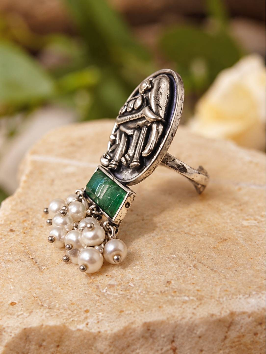 Side profile of oxidised silver elephant ring showing pearl drops and green stone bar on stone surface