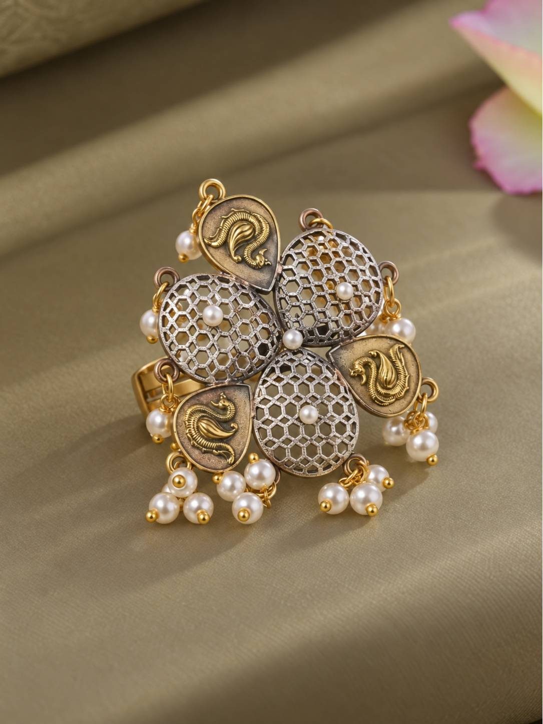 Oxidised silver floral ring with gold paisley motifs, honeycomb jali dome petals and hanging pearl drops on a gold fabric surface