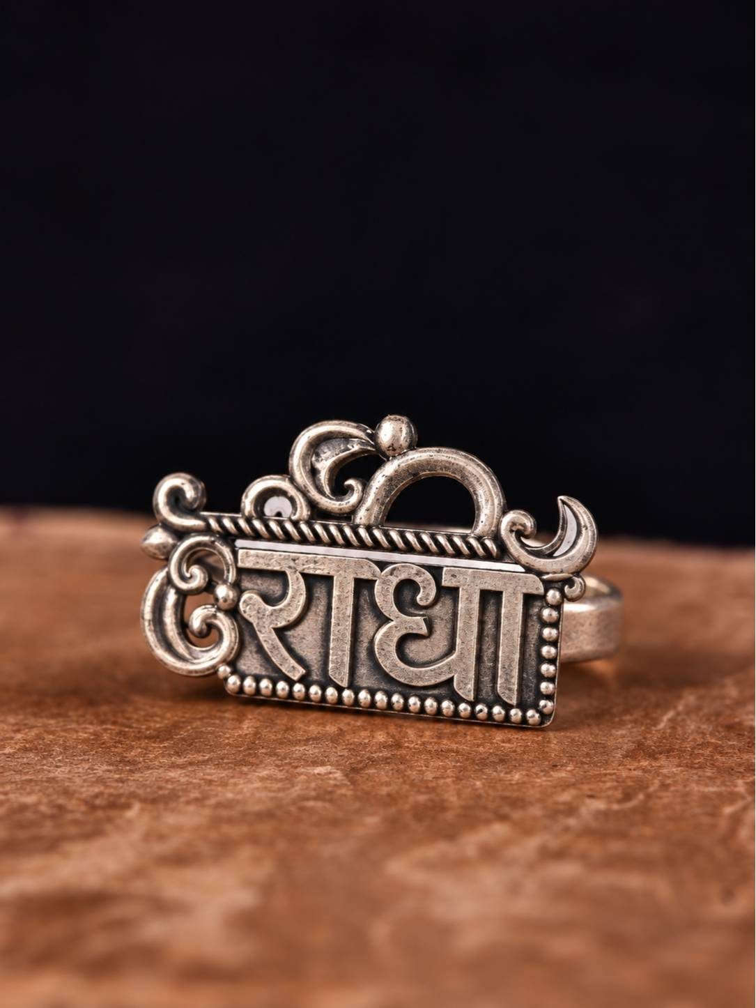 Front view of oxidised silver Radha name plate ring with Om crown and scroll detailing on stone surface