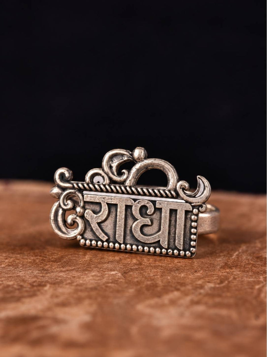 Front view of oxidised silver Radha name plate ring with Om crown and scroll detailing on stone surface