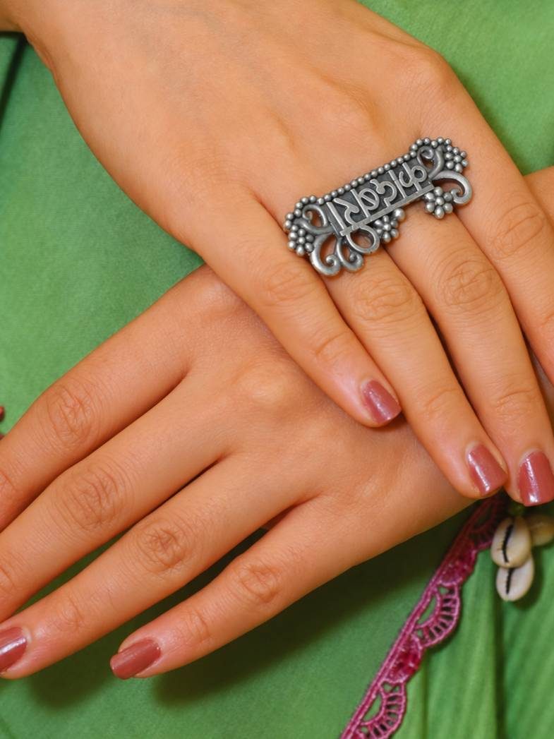 Oxidised silver Kadambari name ring worn on index finger of a hand against a green kurta
