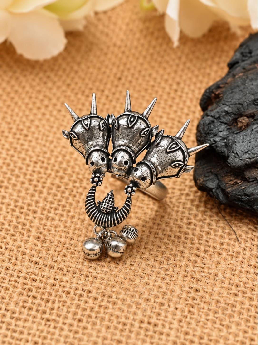 Front view of oxidised silver triple horse head ring with spike crowns and ghungroo bell drops on burlap