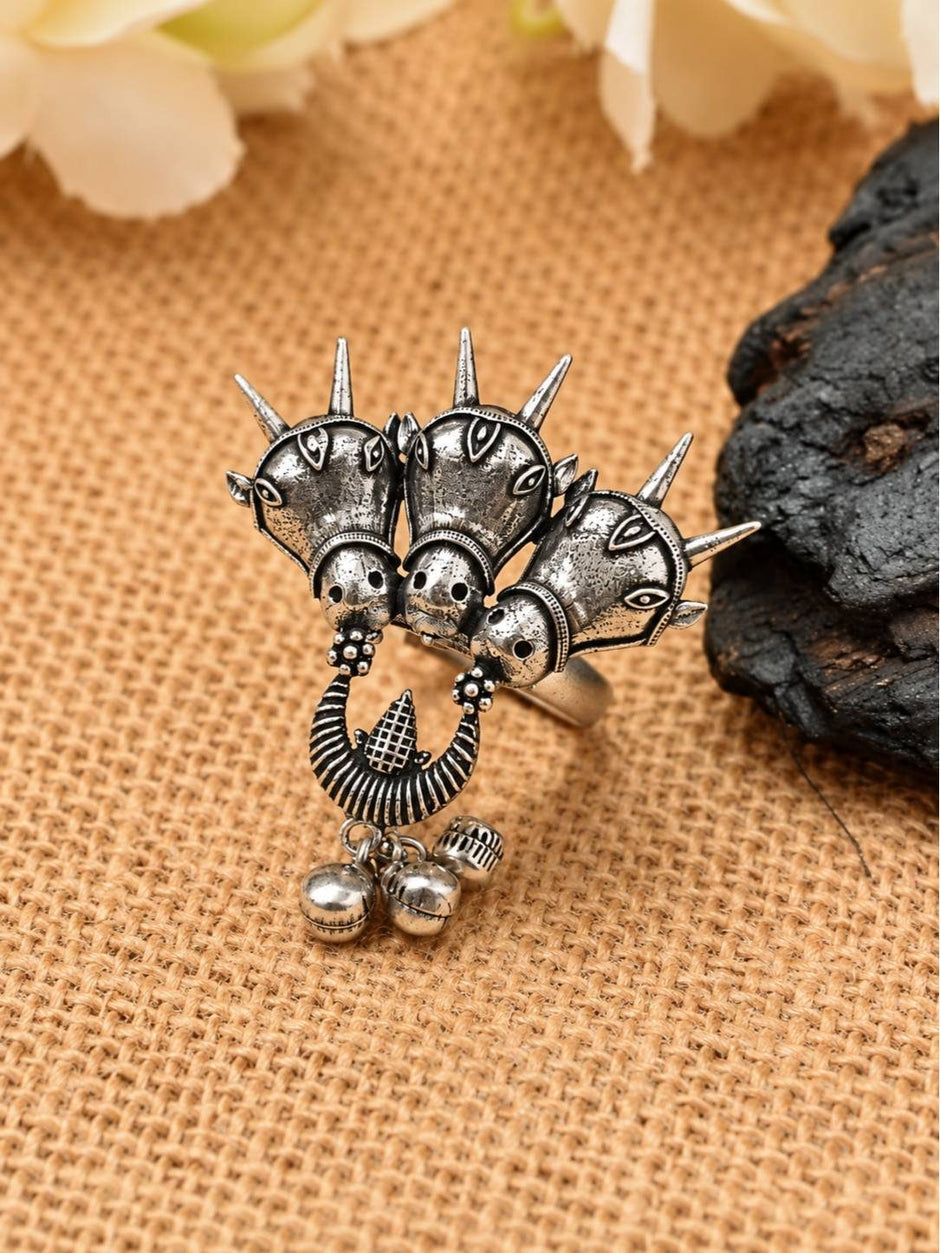 Front view of oxidised silver triple horse head ring with spike crowns and ghungroo bell drops on burlap
