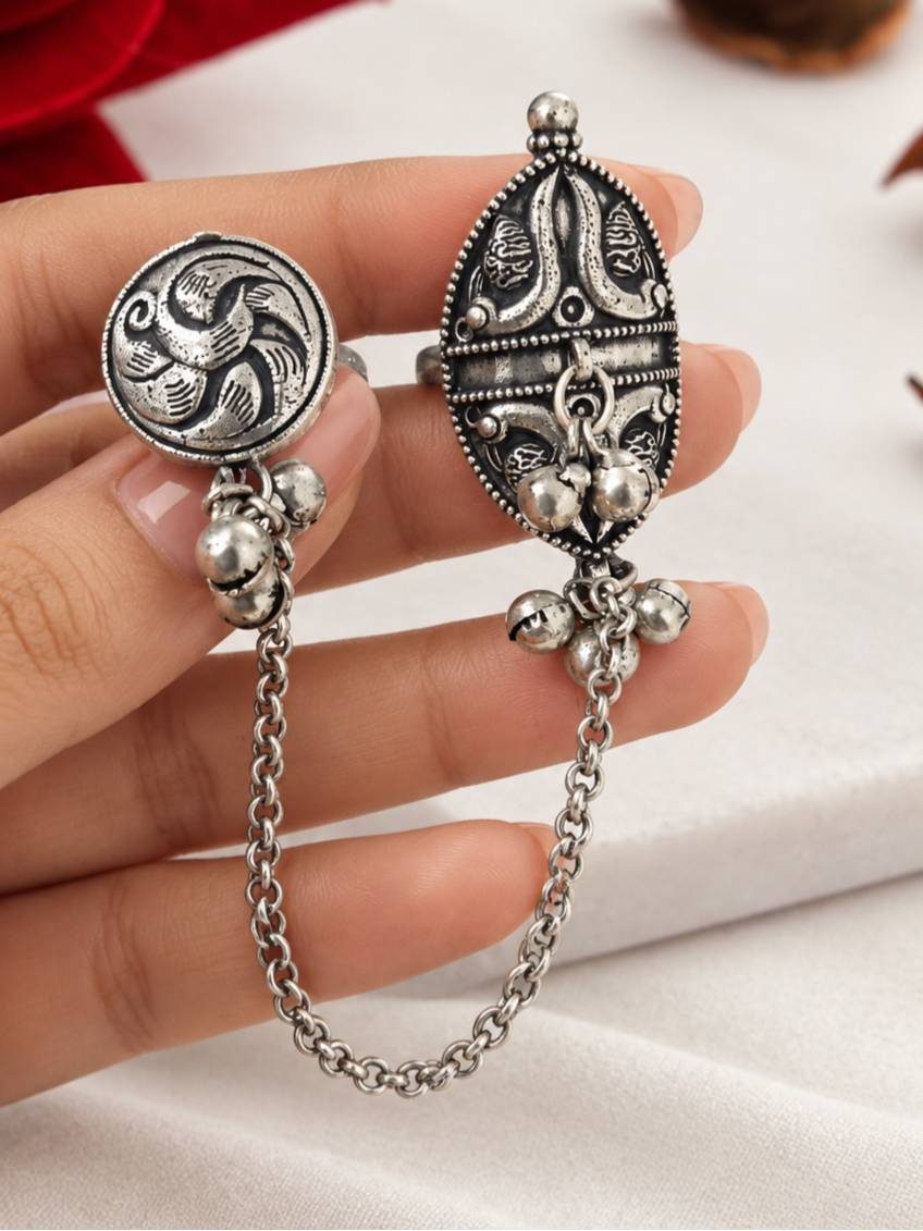 Close-up of oxidised silver dual finger ring held in hand showing floral oval top and circular bird motif ring