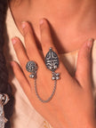 Oxidised silver dual finger ring worn on index and middle fingers of a woman's hand against ethnic fabric background