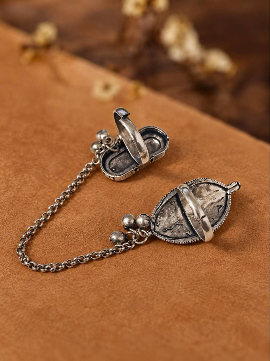 Back view of oxidised silver dual finger rings opened to reveal hollow locket cavities, resting on brown suede