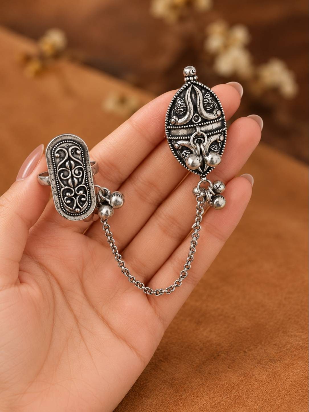 Hand holding oxidised silver dual finger locket ring showing marquise and oblong engraved tops with dangling chain