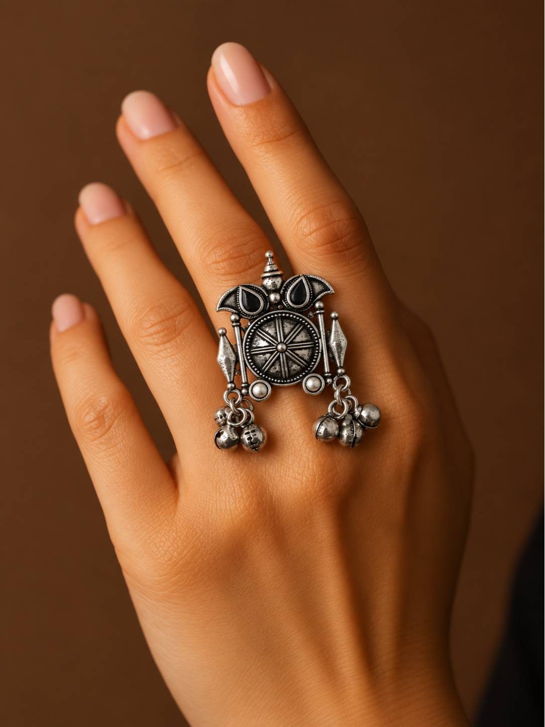 Oxidised silver statement ring worn on middle finger of a woman's hand against a brown background