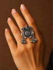 Oxidised silver statement ring worn on middle finger of a woman's hand against a brown background