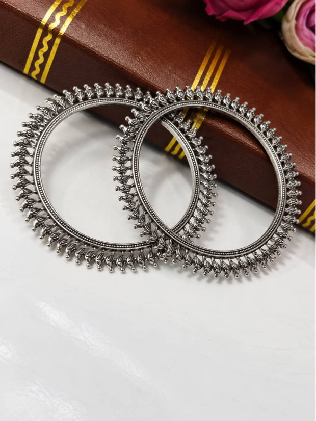 Two oxidised silver floral kada bangles laid flat on a white marble surface beside a brown book and pink roses