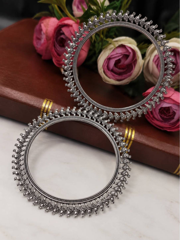 Pair of oxidised silver bird-motif kada bangles resting against a bouquet of pink and cream roses on a brown book