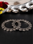 Pair of oxidised silver coin bangles lying flat on a dark surface with flowers and a silver tray in the background