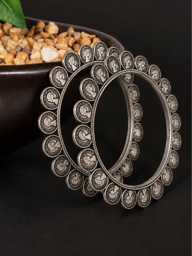 Two oxidised silver coin bangles propped upright showing detailed portrait coin engravings and antique finish close up