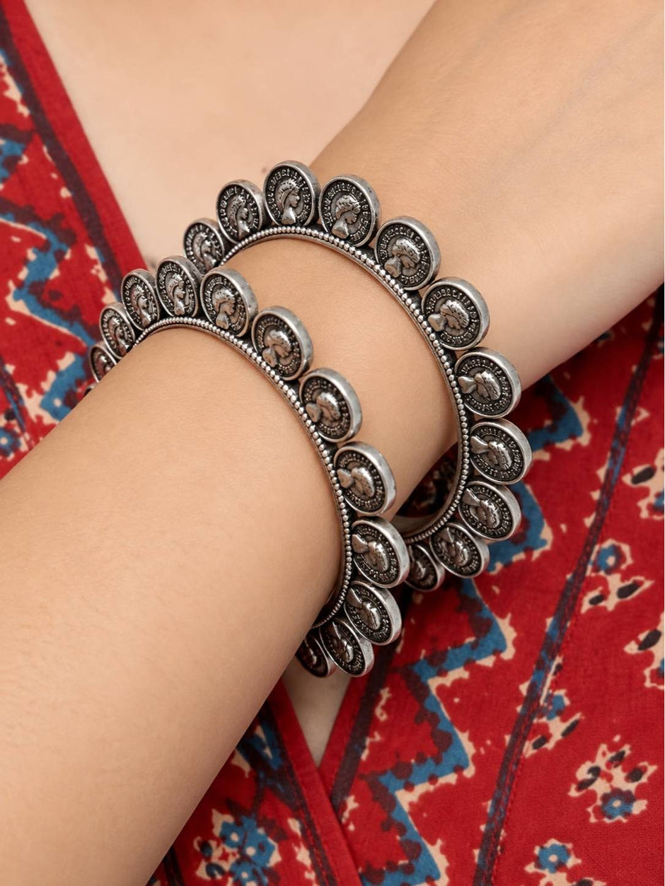 Oxidised silver coin bangles worn stacked on a woman's wrist against a red ajrakh print fabric background