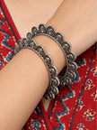 Oxidised silver coin bangles worn stacked on a woman's wrist against a red ajrakh print fabric background