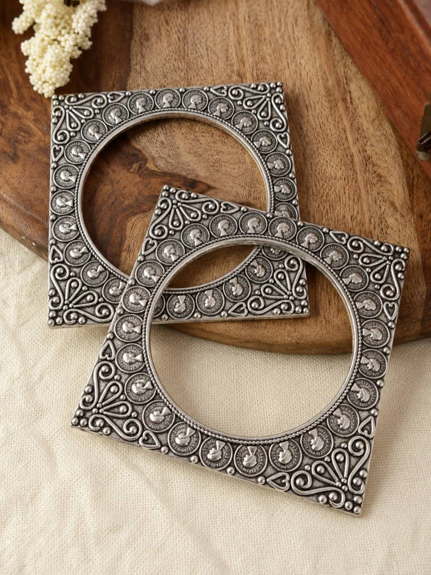 Pair of oxidised silver square coin bangles laid flat on a wooden tray with white flowers in the background
