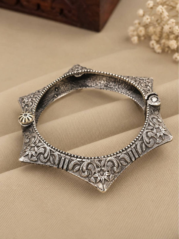 Oxidised silver star-shaped floral kada laid flat on beige fabric with dried flowers in background