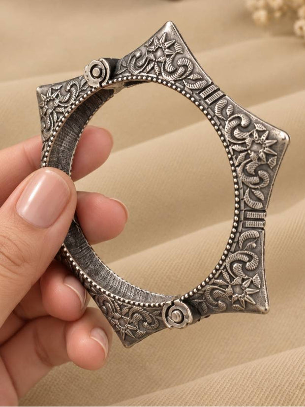 Hand holding oxidised silver angular kada showing engraved vine and floral motifs on inner and outer surface