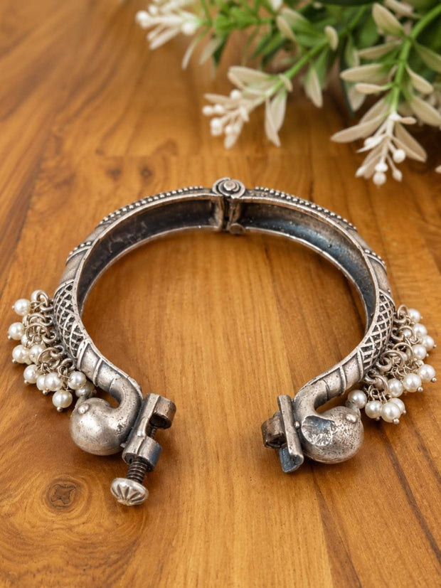 Open clasp view of oxidised silver peacock bangle showing screw-bolt closure mechanism and pearl tassel embellishments on both ends