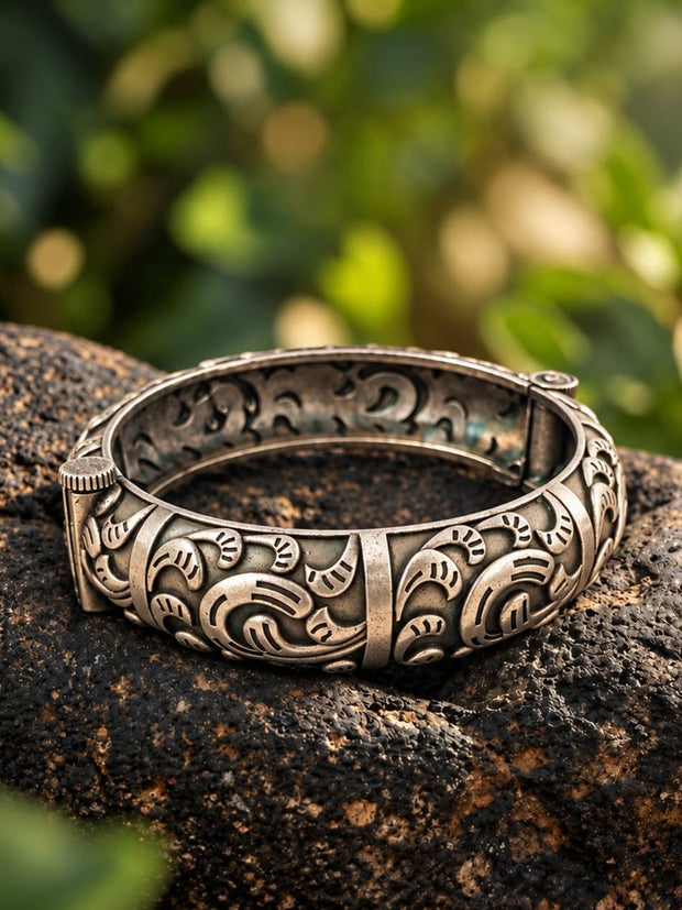Oxidised silver floral kada resting on a dark rock with green bokeh background