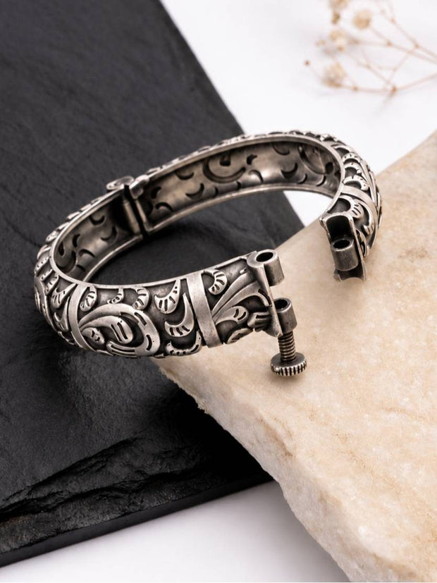 Open hinged oxidised kada showing screw-lock clasp detail on a slate and marble surface