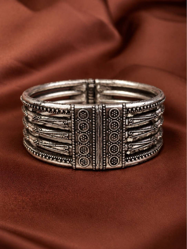 Front view of oxidised silver multi-band cuff kada showing engraved circle motif clasp panels on rust fabric