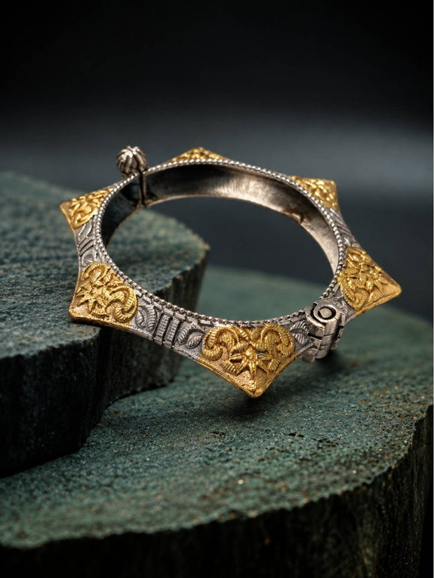Front view of gold and oxidised silver engraved floral kada placed on textured green stone blocks