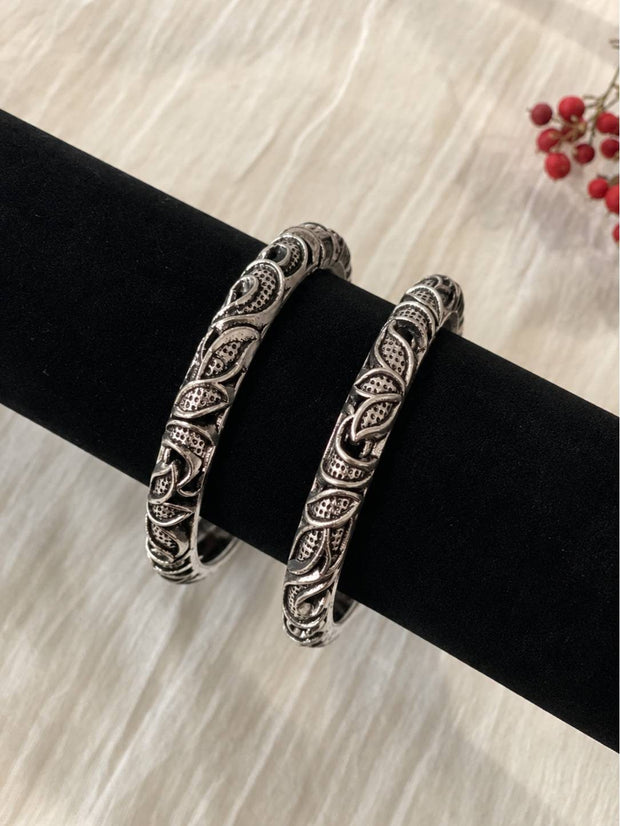 Pair of oxidised silver carved kada bangles displayed upright on a black velvet jewellery stand