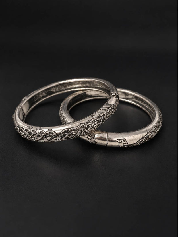 Pair of oxidised silver hinged kada bangles laid flat on a dark surface showing floral engraving