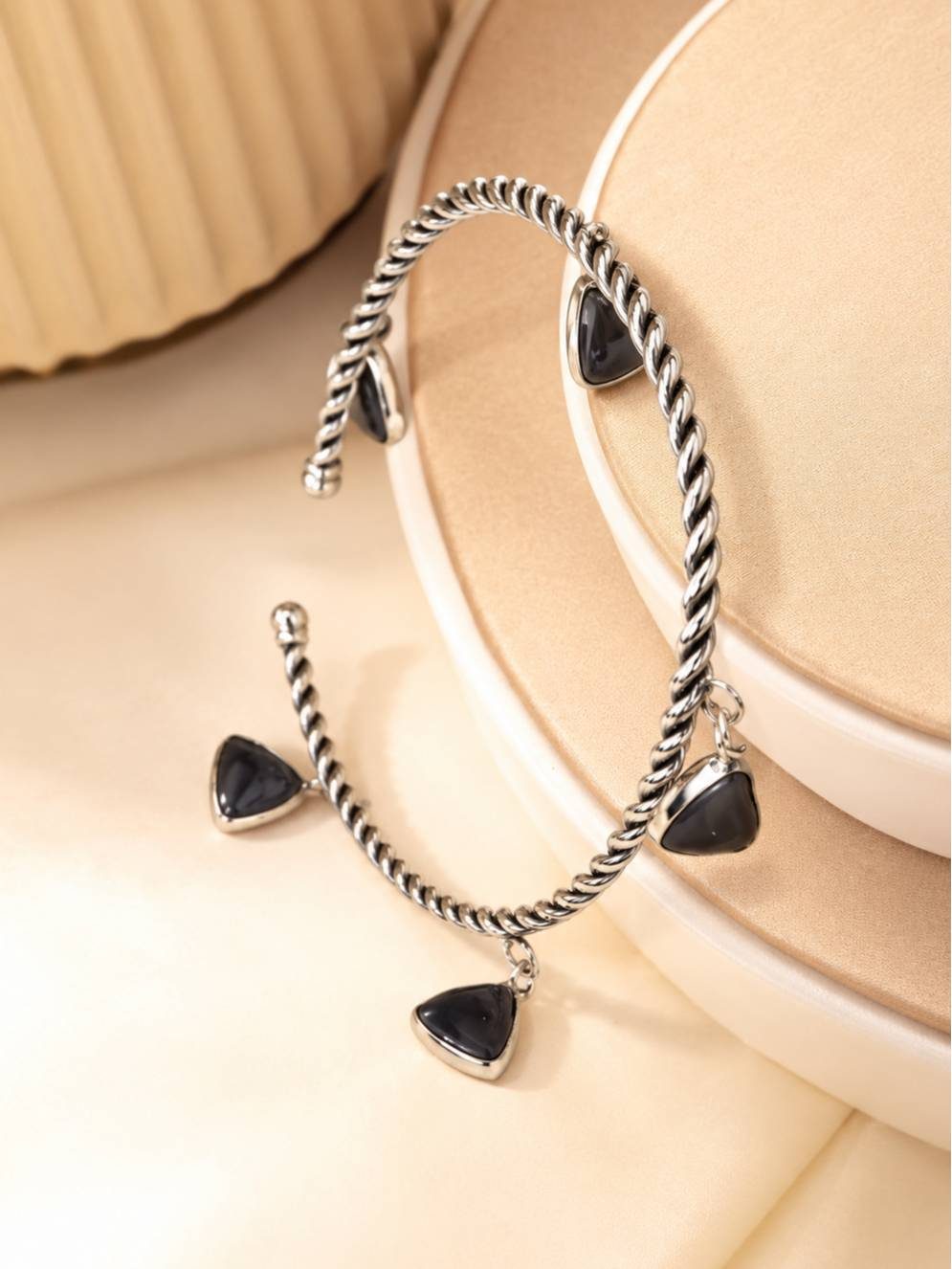 Pair of oxidised silver twisted charm bracelets propped upright against a layered beige display stand