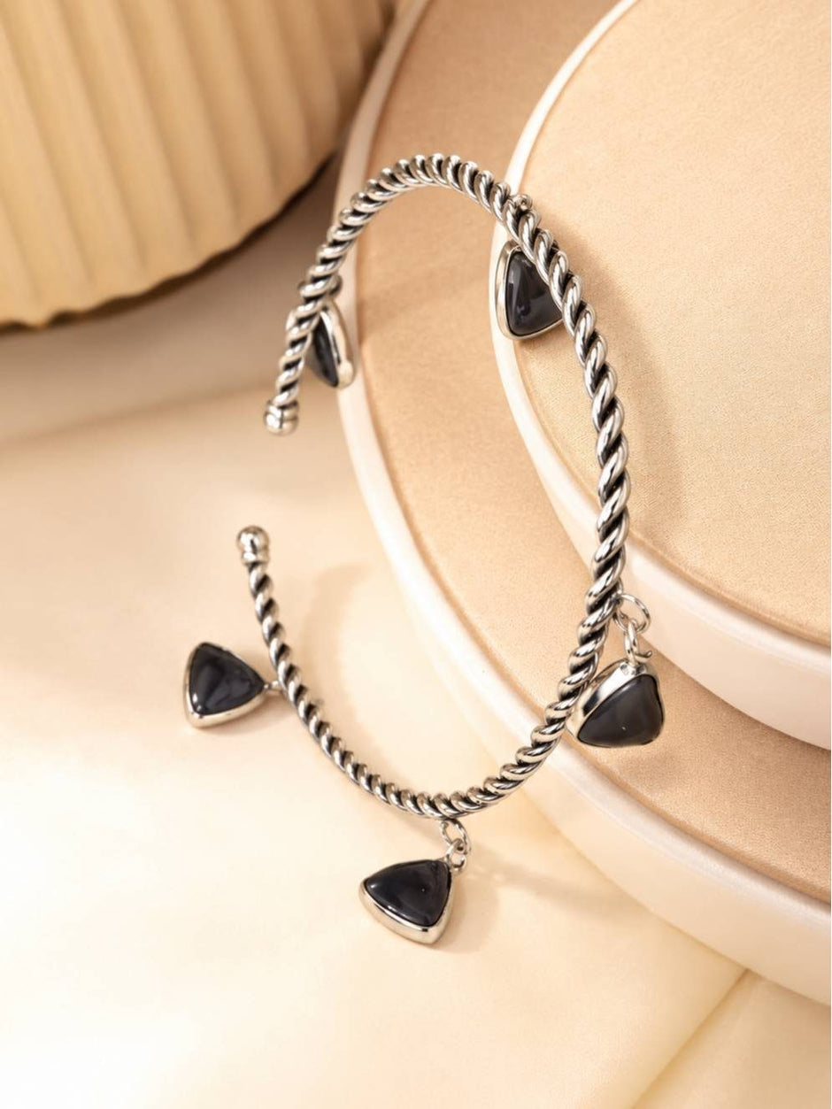Pair of oxidised silver twisted charm bracelets propped upright against a layered beige display stand
