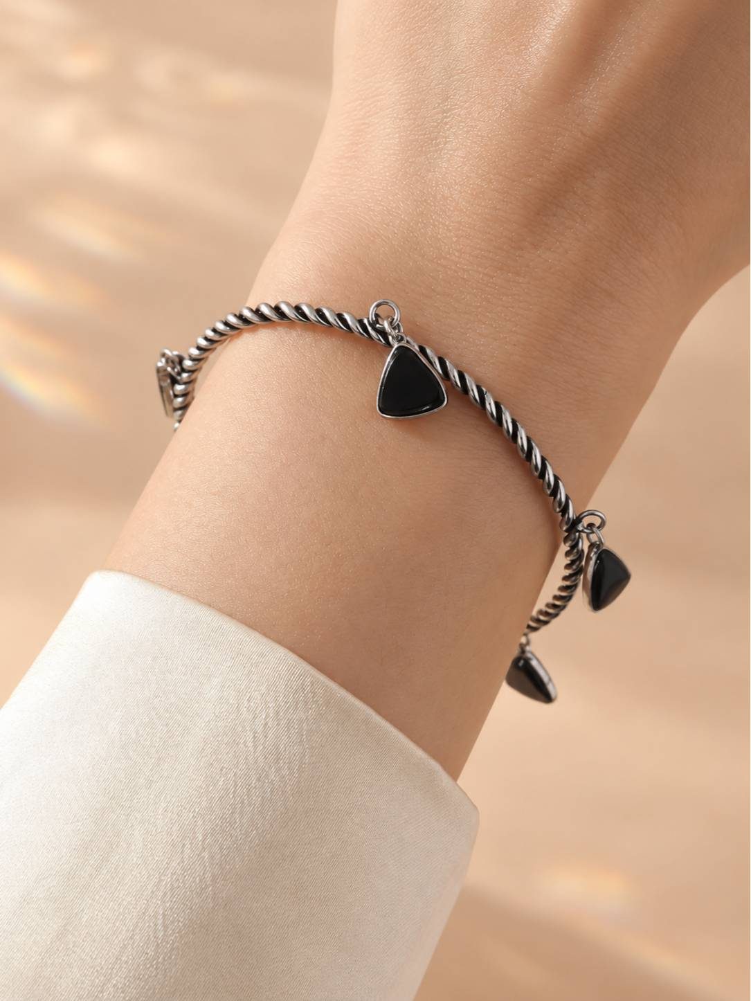 Oxidised silver twisted cuff bracelet with black triangle charms worn on a woman's wrist over a white sleeve