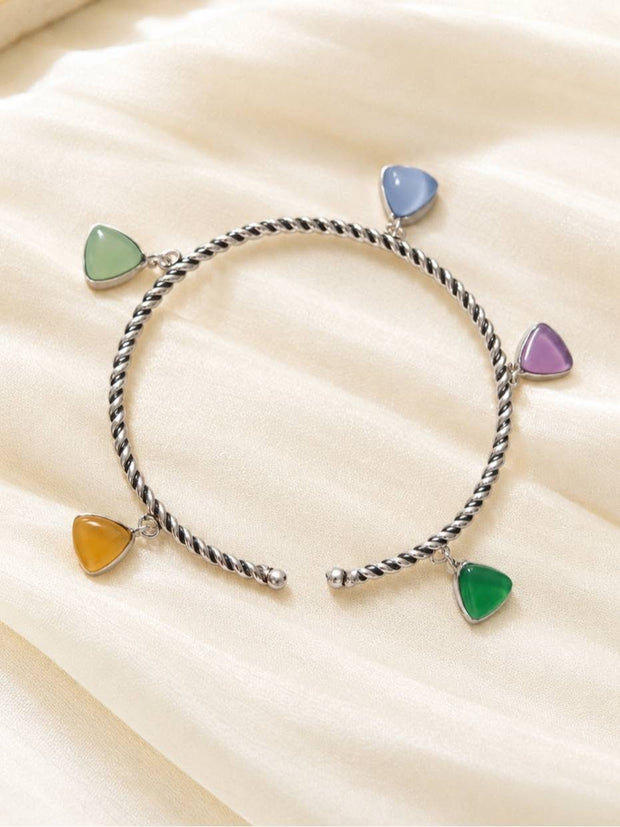 Oxidised silver twisted cuff bracelet laid flat showing five multicolour triangle stone charms on cream fabric
