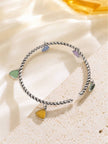 Multicolour stone charm cuff bracelet resting on a sandy textured surface with warm golden light behind