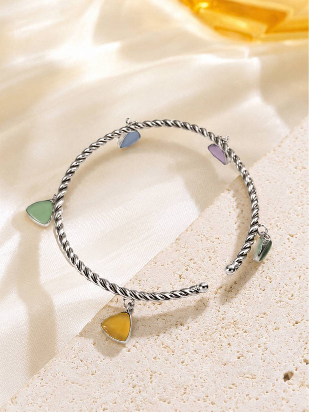 Multicolour stone charm cuff bracelet resting on a sandy textured surface with warm golden light behind