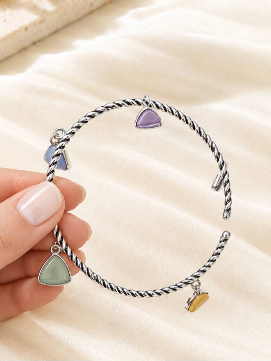 Close-up of a hand holding an open oxidised silver cuff bracelet showing green, blue, lavender and amber triangle charms