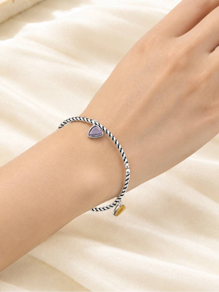 Oxidised silver multicolour charm cuff bracelet worn on a woman's wrist against a soft cream satin background