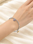 Oxidised silver multicolour charm cuff bracelet worn on a woman's wrist against a soft cream satin background