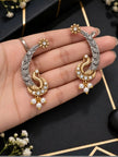 Both peacock ear cuffs held in an open palm showing gold-tone peacock and silver leaf engraving