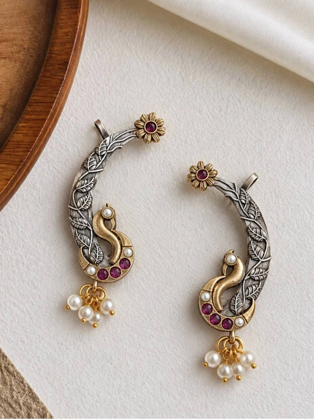 Pair of oxidised silver peacock ear cuff earrings with ruby stones and pearl drops on white surface