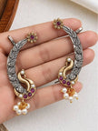 Both peacock ear cuff earrings held in a woman's palm showing front detail and leaf engravings
