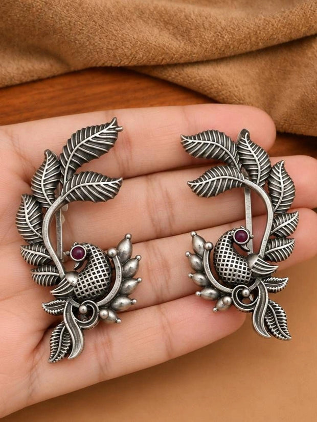 Pair of oxidised silver bird ear cuff earrings with red stone held in a palm