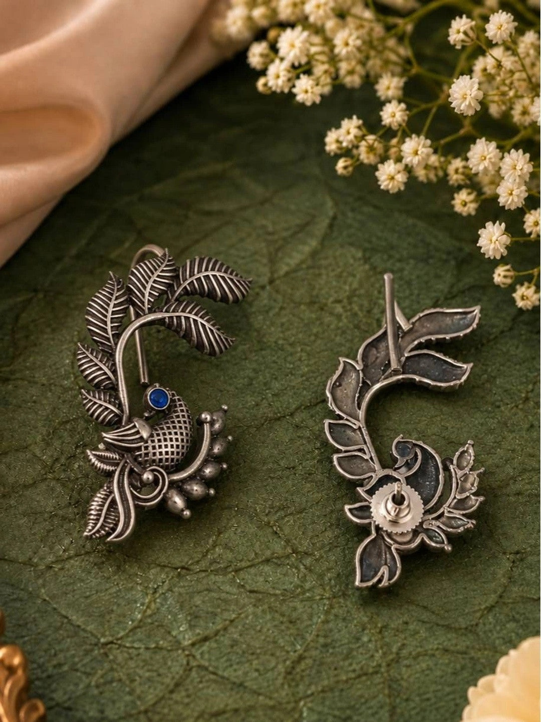 Front and back view of oxidised silver peacock ear cuff earrings with blue stone on green surface