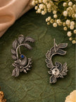 Front and back view of oxidised silver peacock ear cuff earrings with blue stone on green surface