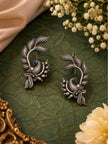 Pair of oxidised silver peacock ear cuff earrings laid flat on dark green leather surface
