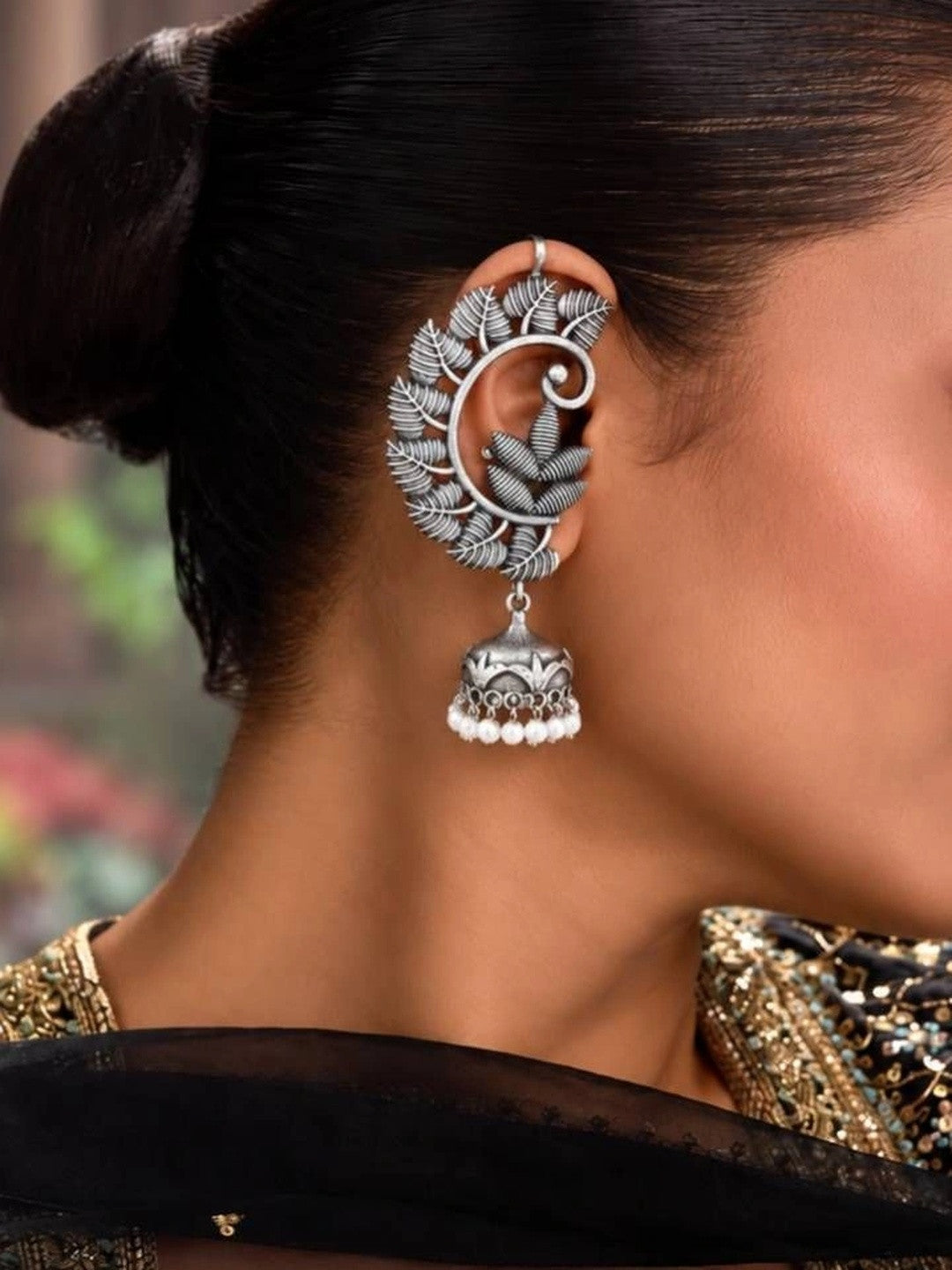 Oxidised silver leaf chandbali jhumka earring worn on a woman's ear, shown from behind against a blurred green background