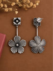 Front and back view of oxidised silver floral drop earrings on a brown surface with dried flowers