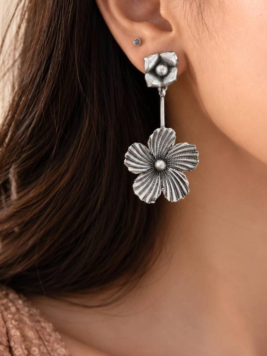 Oxidised silver five-petal floral drop earring worn on a woman's ear showing full length