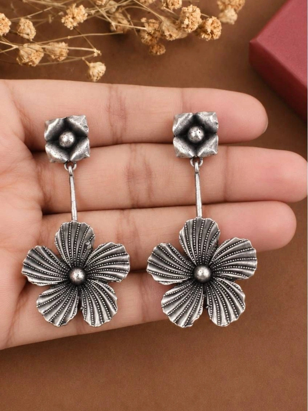 Pair of oxidised silver flower drop earrings resting on an open palm for size reference