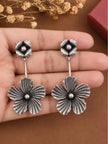 Pair of oxidised silver flower drop earrings resting on an open palm for size reference
